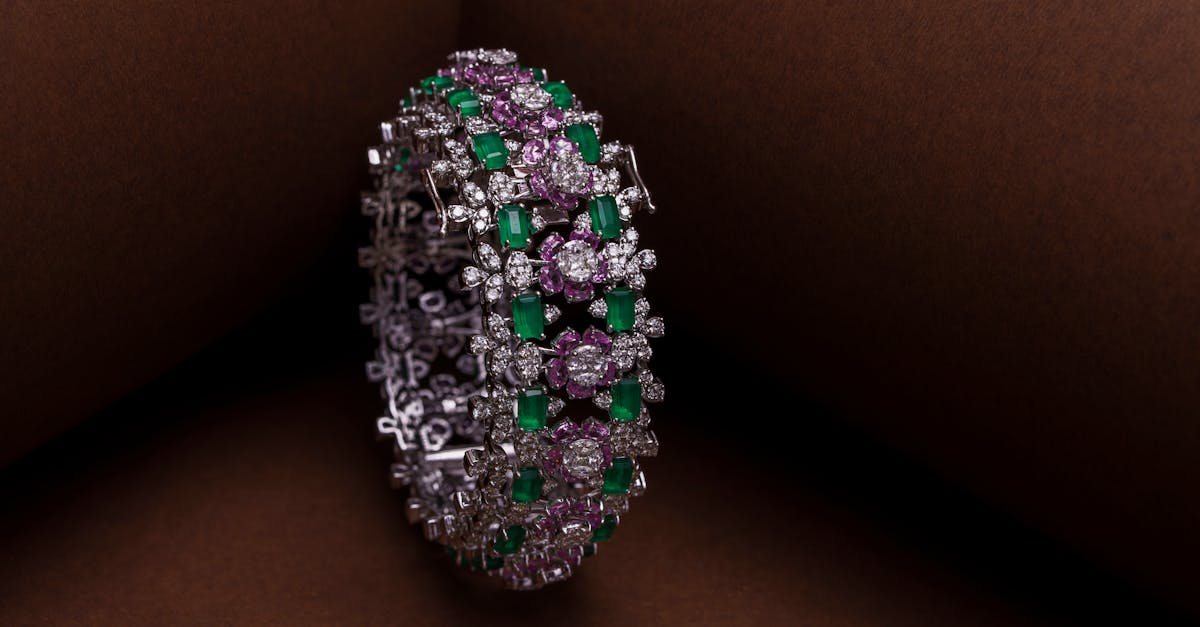 Luxury diamond bracelet with green and pink gemstones displayed on a brown surface.
